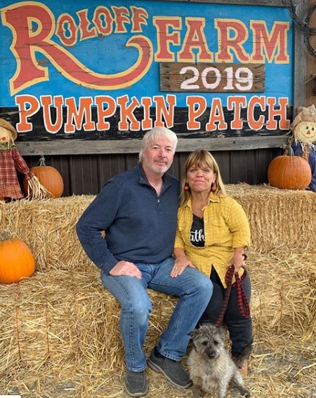 Amy Roloff and Chris Marek on the Roloff Farm. Amy is holding a dog on the leash while facing the camera.