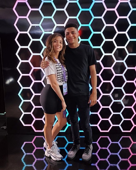 Myth wearing a black T-shirt and black pants and grey shoes, with his right arm around Poki's right shoulder. Poki s sporting a white shirt with the word "Pokimane" written in multiple lines on it and a black skirt while sporting white shoes.