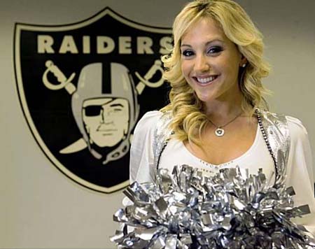 Emily Copagno in front of the Raiders logo, wearing a cheerleader's dress.