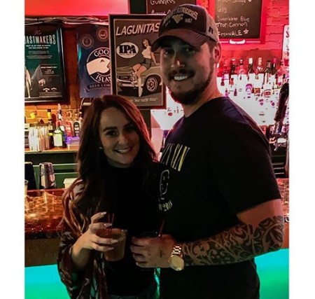 Leah and Jeremy posing for the camera while holding a drink on their hand.