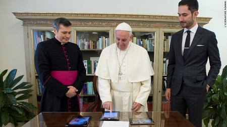 The Pope (right) pointing his finger on an iPad to post beside Kevin (right) and an archbishop.