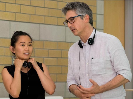 Hong Chau (left) with headphones around her neck and her hands on the headphones wearing black top. Alexander Payne (right) in a white shirt with headphones around his neck and scratching his hand.