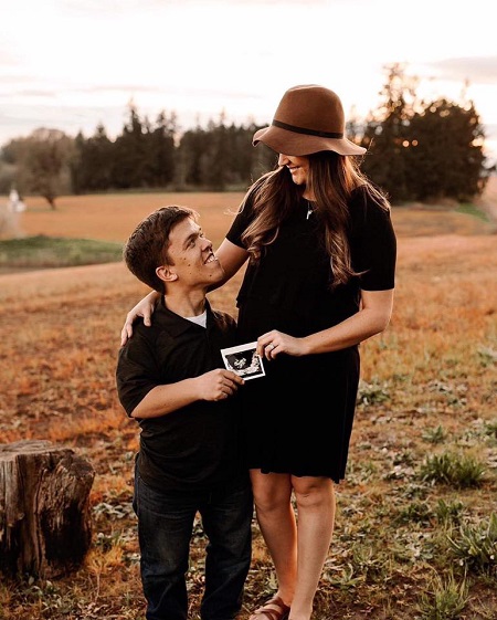 Zach and Tori looking at each other, both holding each ends of an ultrasound picture. Both standing.