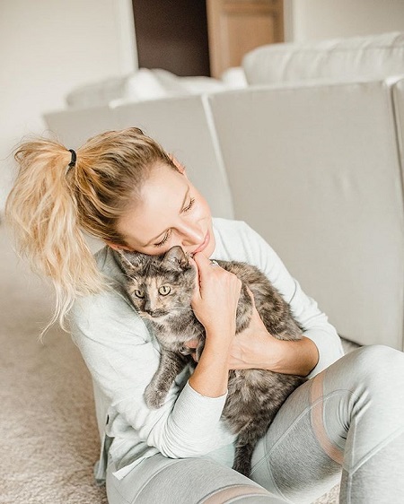 Emily snuggling her cat when sitting in on the carpet floor. The setup is all white except the cat.