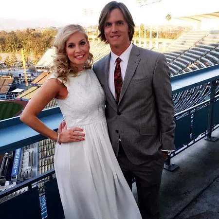 Emily (left) in white dress and Zack (right) in a grey suit posing in the stadium stands.