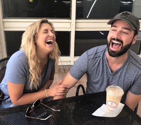 Gina and Mullen laughing as they are sitting in some cafe.