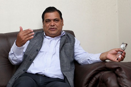 Mahara sitting on a couch, a photo clicked as he is speaking with his right hand raised to his mouth level and spectacle on the other hand, resting on the couch.