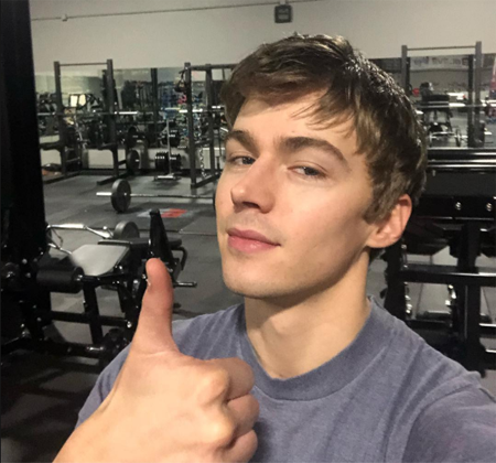 Miles Heizer inside a gym, giving a thumbs up.