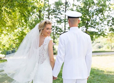 Liz and her husband standing away from the camera holding hands as only Liz looks back at the camera.