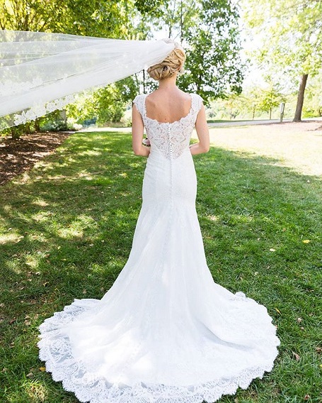 Liz standing & facing away from the camera with her veil lifted from the back by an unseen person.