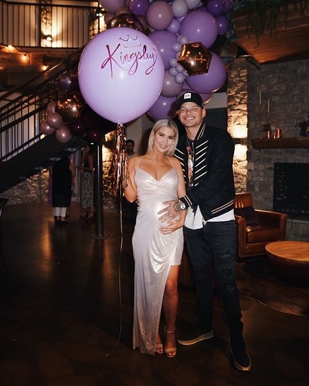 Kane touching Katelyn's baby bump while she is holding the balloon with 'Kingsley' written on it.