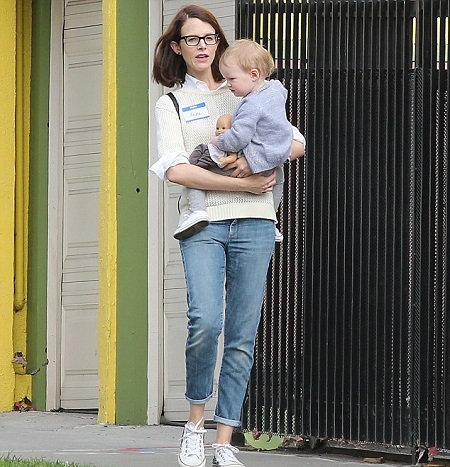 Anne carrying her daughter in her arms as they walk outdoors.