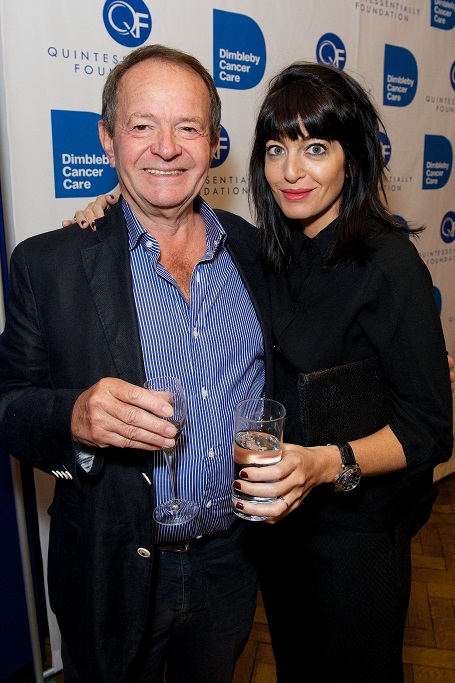 Claudia puts her right hand on Barry's right shoulder as they smile at the camera holding water glasses.