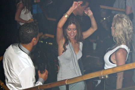 Kathryn Mayorga dancing (middle) with her arms in the air as Ronaldo (left, face not seen) watches her from beside her.