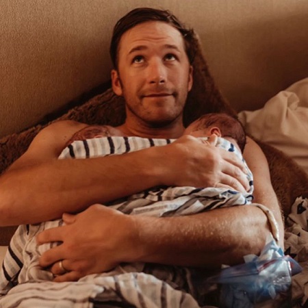 Bode Miller resting on the bed holding the twins wrapped with a towel in his arms.