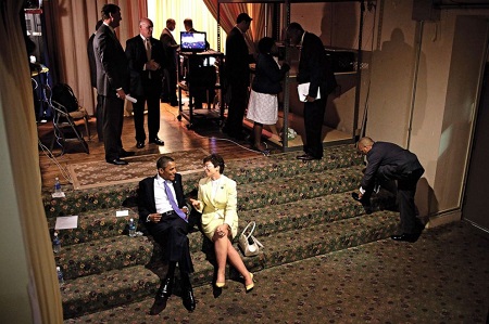 Valerie Jarrett kicks back on the stairs with President Obama before an event. Both looking at each other talking about something and smiling.