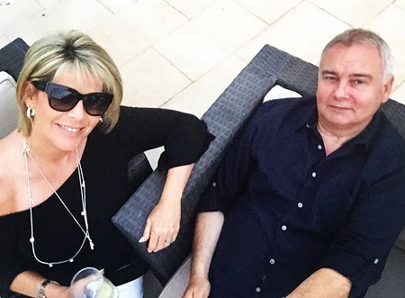 Eamonn sitting on a chair leaning back as Ruth sits in another chair beside him, both looking up at the camera while wearing black dresses.