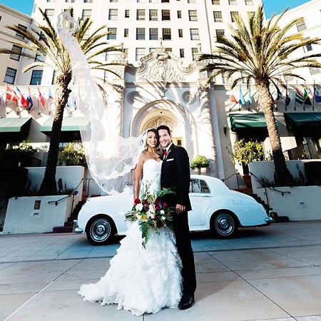 Liana and David on their wedding day in their wedding dresses, in front of a white bug car.