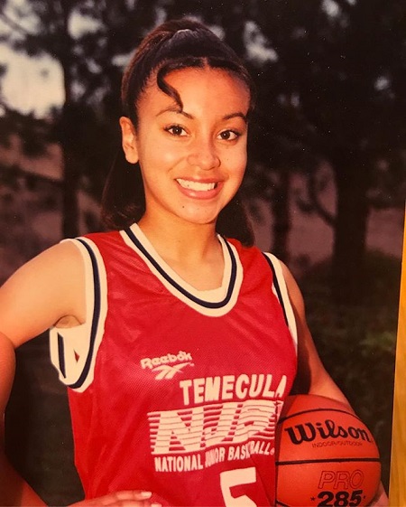 Young Liana in a basketball dress smiling, holding a basketball in her left hand.