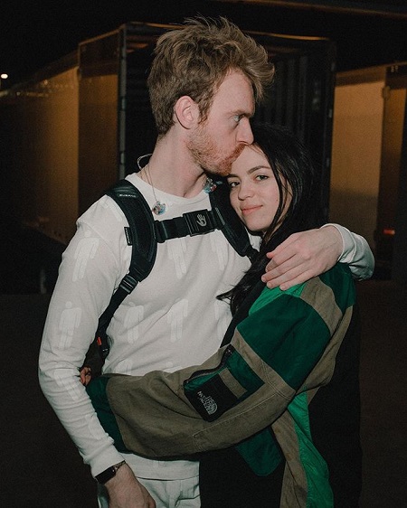 Finneas kissing Claudia on the forehead as she is smiling at the camera hugging him.