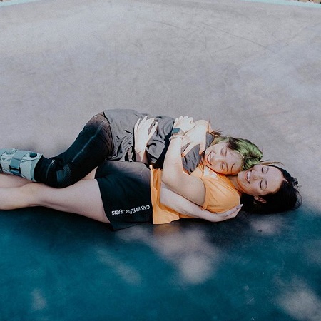 Billie and Claudia hugging each other as they lie of the floor smiling and eyes closed..