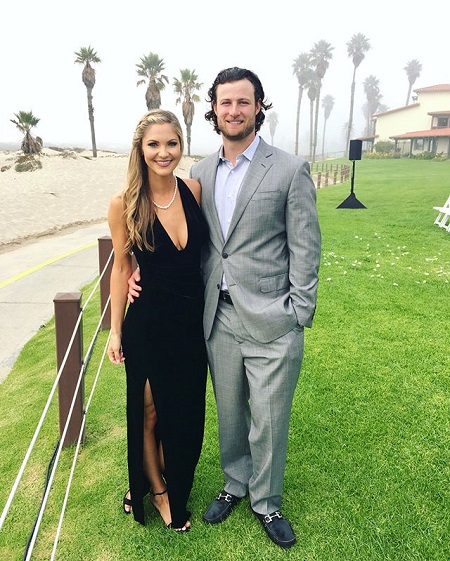 Gerrit Cole with his arm around wife Amy Crawford smiling at the camera. He in a grey suit and she is in a revealing black dress.