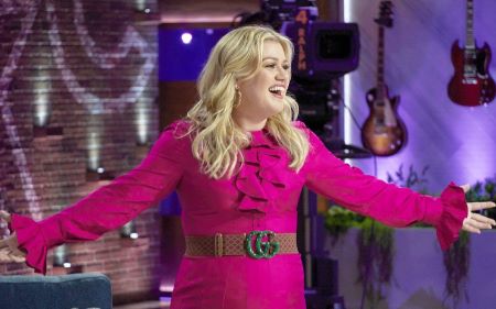 Kelly Clarkson spreading her arms and laughing in a pink dress on her show.