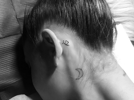Ariana resting head on pillow, bee and crescent moon tattoos are seen, but not her face.
