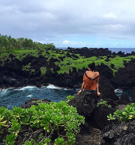 Alisha Wainwright sitting on Lava Rocks in Hawaii facing her back.