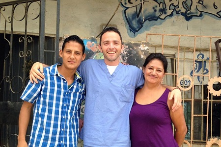 Jimmy Karz in the center smiling at the camera in a nurse dress with his hands on two people on either  side's shoulders.