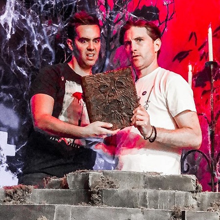 Michael Carbonaro and Peter Stickles holding a horror book and looking horrified.