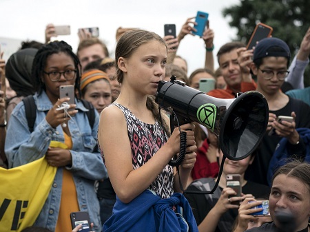 Greta speaking with a boom mic while people surrounding her are taking her pictures and videos on their phones.