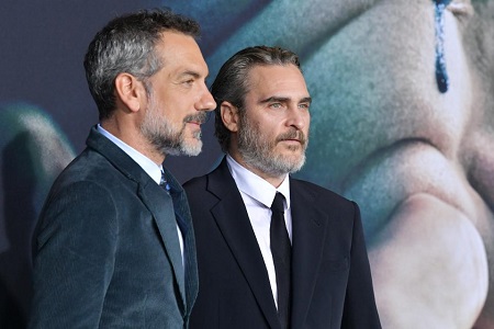 Joaquin Phoenix (right) and Todd Phillips facing sideways (right) looking at two different cameras in suits.