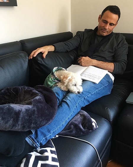 Keven Undergaro in a sofa with his dog resting on his knees.