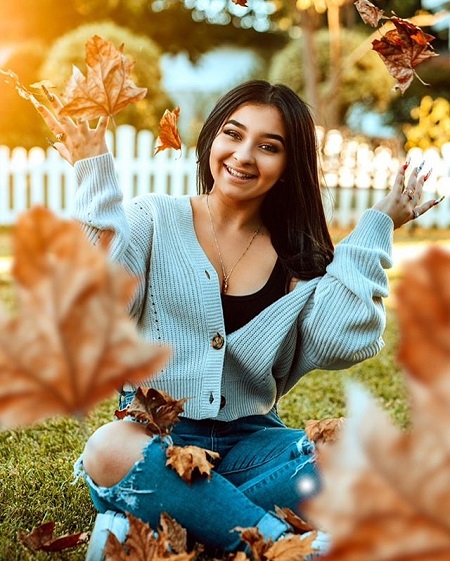 Danielle Cohn sitting on the ground and throwing leaves in the air.