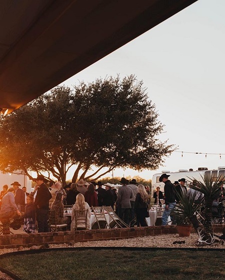 The moment of wedding reception captured from afar, people sitting and standing while surrounding the ranch tree.