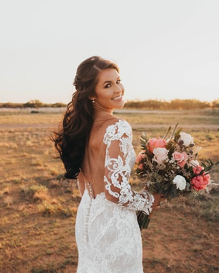 Kinsel holding the wedding bouquet facing her back with head turned back to the camera.