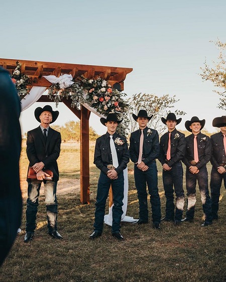 The groomsmen at the Jess Lockwood + Hailey Kinsel Wedding dressed like cowboys like the bride, standing with hands crossed at the alter.