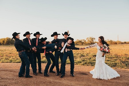 The groomsmen carrying the groom, Lockwood, as he extends his hand out to reach the bride, Kinsel, holding a bouquet.