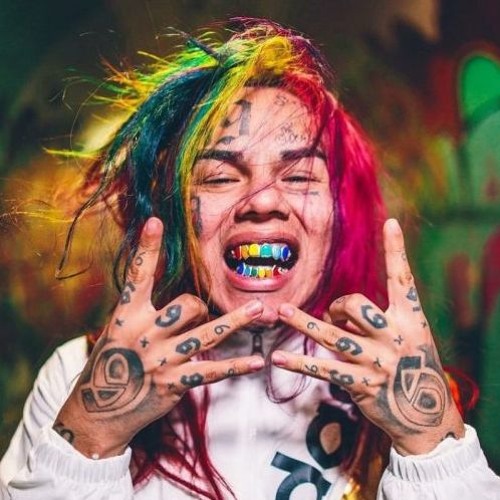 tekashi with rainbow hari and tatted body, smiling showing off his rainbow teeth grills 