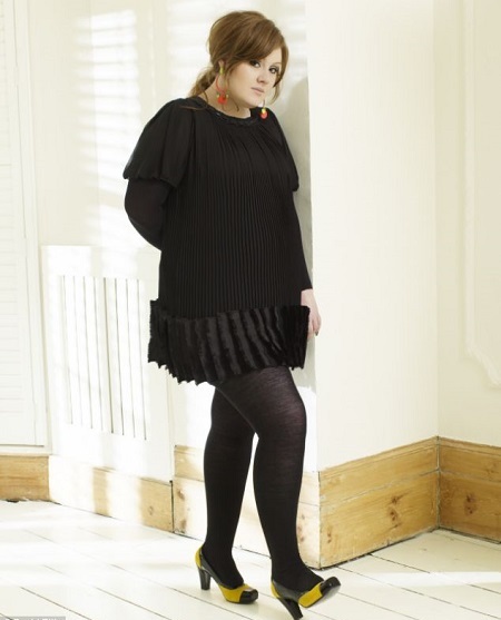 Adele in all black posing while leaning on a wall.