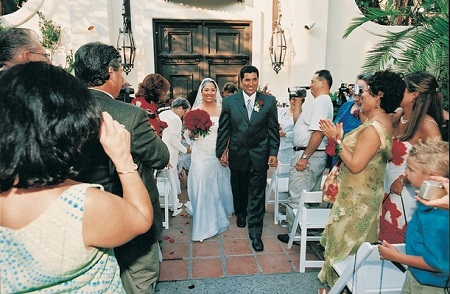 Lynette Romero and husband David Angulo walking the outdoor aisle on their wedding day. Lynette holding the bouquet and smiling with husband.