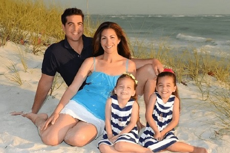 Jesse Watters, Noelle Watters and their two daughters in matching striped outfit sitting on the sand of the beach.