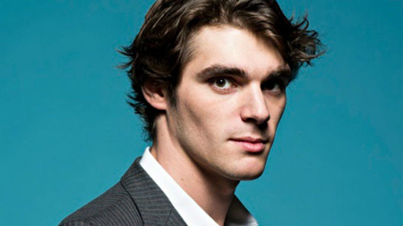 RJ Mitte in a suit, with his hair combed back, looks at the camera to take a profile shot.