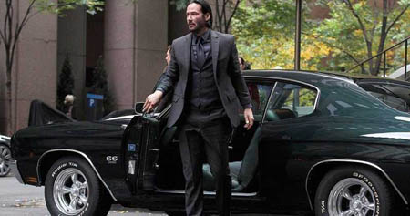Keanu as John Wick getting out of his car in all black suit and tie.