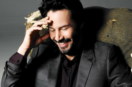 Keanu looks down, with one hand on his head and laughs.
