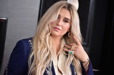 Kesha uses her left hand to move her blonde hair.