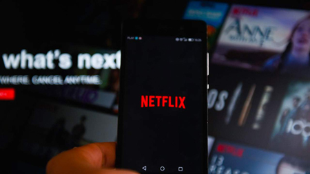 Mobile phone shows the Netflix logo as the background image also shows the Netflix front page.