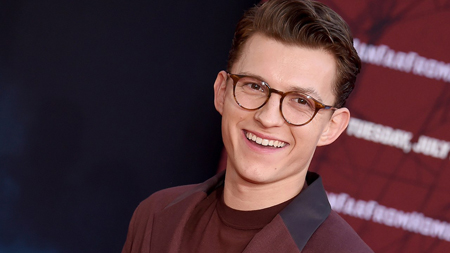 Tom Holland wearing glasses smiles to take a photo.