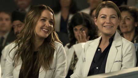 Ellen Pompeo is seen smiling on a auditorium, wearing doctor's clothes.